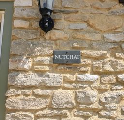 Stone wall with a black sign reading NUTCHAT and a lantern above the sign at Nutchat Barn in Burford