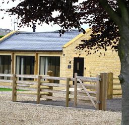 A stone house with large glass doors and a wooden fence in front at Court Hayes Farm Barns Bourton-On-The-Water