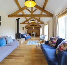 A long living room with wooden beams on the ceiling sofas and a stove at Court Hayes Farm Barns in Bourton-On-The-Water