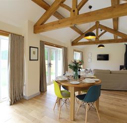 A dining area with a round wooden table and colorful chairs next to a living area with a sofa and a wood stove at Park Bothy in Wyck Rissington