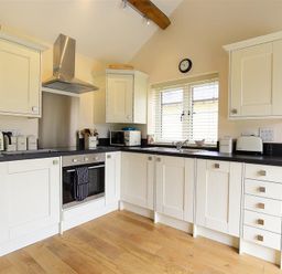 A kitchen with white cabinets black countertops and wooden floor at Park Bothy in Wyck Rissington