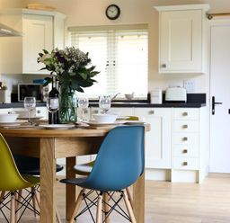 A kitchen with a wooden dining table set for four with colorful chairs and a flower vase at Park Bothy Wyck Rissington