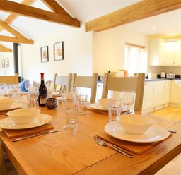 A dining table set with bowls plates glasses and cutlery in a kitchen with wooden beams at Park Stables Wyck Beacon near Bourton-on-the-Water
