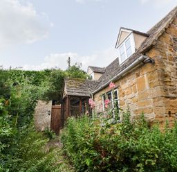 A stone cottage with a garden path surrounded by plants and flowers at Hadcroft Cottage in Aston Magna