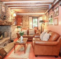 A sitting room with leather sofas a stone fireplace and wooden beams at Hadcroft Cottage in Aston Magna