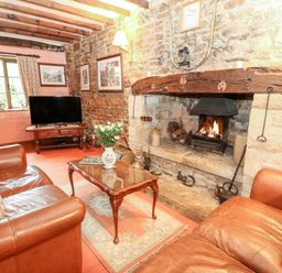 A sitting room with leather sofas a wooden coffee table and a fireplace at Hadcroft Cottage in Aston Magna