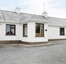 A single-story house with white walls and brown trim with multiple windows and two chimneys at Daffodil Cottage in Grange County Sligo