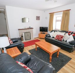 A living room with black leather sofas a wooden coffee table a fireplace and a television at Daffodil Cottage in Grange County Sligo