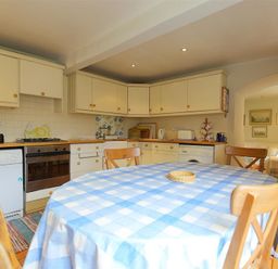 A kitchen with cream cabinets a blue checkered tablecloth on a round table and wooden chairs at The Mews Cottage in Tisbury