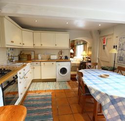 A kitchen with wooden countertops cabinets a washing machine and a dining table with a blue checkered tablecloth at The Mews Cottage in Tisbury