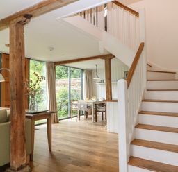 A dining area with a table and chairs next to large windows and a staircase with wooden steps at The Cart Barn in Ridge near Chilmark