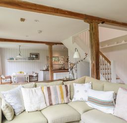 A living room with a light green sectional sofa with pillows and wooden beams in an open space with a dining area and kitchen at The Cart Barn Ridge near Chilmark