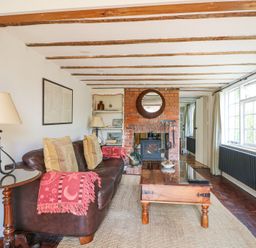 A living room with a leather sofa pillows a wooden coffee table and a brick fireplace at Gun Hill Cottage in Heathfield