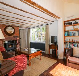 A living room with a brick fireplace wooden coffee table bookshelf and a brown armchair at Gun Hill Cottage in Heathfield