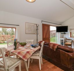 A dining area with a table and chairs next to a living area with a leather sofa and a wall-mounted TV at Russet in Martin
