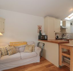 A small living area with a beige sofa and pillows next to a kitchen with cabinets and a wooden floor at Russet in Martin