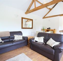 A living room with two brown leather sofas a wooden coffee table and exposed wooden ceiling beams at The Old Dairy in Flaxley