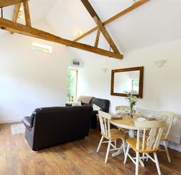 A living room with a wooden dining table with chairs and black sofas at The Old Dairy in Flaxley