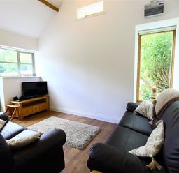 A living room with two black leather sofas a wooden TV stand with a television and windows showing greenery outside at The Old Dairy in Flaxley