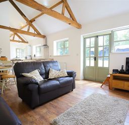 A living room with wooden beams a black leather sofa a wooden dining table and green French doors at The Old Dairy in Flaxley