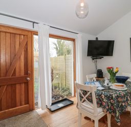 A dining area with wooden door table with floral tablecloth white chairs wall mounted television and a framed picture at Pippin in Martin