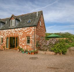 A brick house with a slate roof potted plants on gravel outside and a green umbrella in the garden at The Coach House in Lympstone