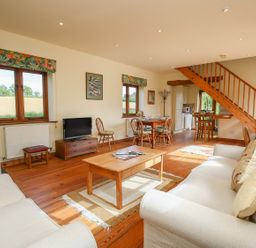 A living room with sofas coffee table dining table and wooden staircase at The Coach House in Lympstone
