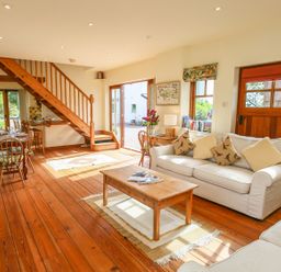 A living room with wooden furniture a sofa with cushions a coffee table and a staircase at The Coach House in Lympstone