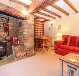 A living room with a red sofa a wooden coffee table a small dining table and stone fireplace at Spring Cottage in Wroxton