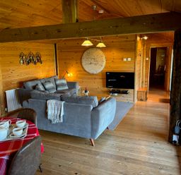 A living room with grey sofas a wall-mounted tv and a dining table with a red tablecloth at Treetops in Woody Bay