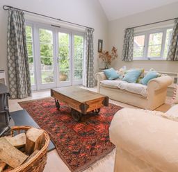 A living room with sofas, a wooden coffee table on a patterned rug, a basket with firewood and a TV at Bridge Studio in Broad Chalke