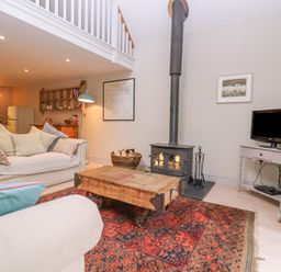 A living room with sofas a wooden coffee table a rug a wood stove and a television at Bridge Studio in Broad Chalke