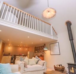 A living room with a wood stove and a staircase railing above at Bridge Studio in Broad Chalke