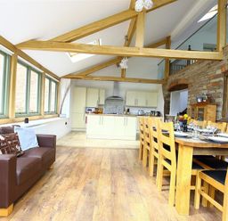 An open kitchen and dining area with wooden beams a brown sofa and large dining table at The Old Mill in Flaxley