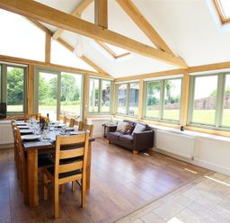 A dining room with a wooden table set for twelve and a sofa by windows at The Old Mill in Flaxley