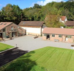 A courtyard with stone buildings surrounded by grass and trees at The Old Mill in Flaxley