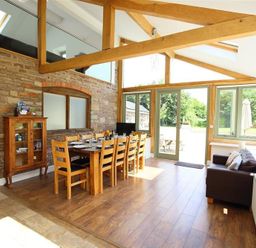 A dining area with a wooden table set for eight and a small sofa near large windows at The Old Mill in Flaxley