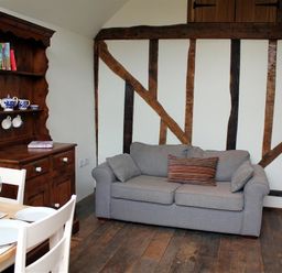 A room with a gray sofa, wooden cabinet with blue and white tea set, and a dining table with white chairs at Pop's Barn in Downton