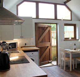 A kitchen with wooden countertop a kettle microwave stove and a dining table with chairs near a wooden door at Pops Barn in Downton