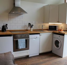 A kitchen with wooden countertops white cabinets a stove a dishwasher a washing machine a microwave and a kettle at Pops Barn in Downton
