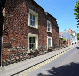 A brick building with four windows along a street with parked cars and trees at Rojoy in Salisbury
