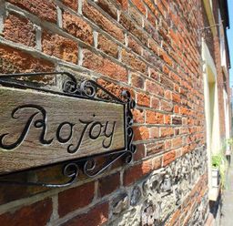 A wooden sign with Rojoy on a brick wall outside a building at Rojoy Salisbury