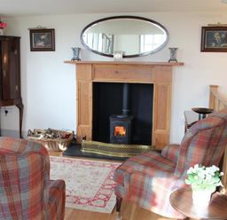 A sitting area with plaid armchairs, a fireplace with firewood basket, an oval mirror, paintings, and a cabinet at The Folly at Castlebridge in Mere
