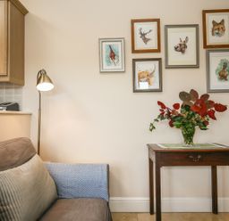 A small wooden table with a vase of leaves and flowers next to a gray couch and a floor lamp with framed animal pictures on the wall at West Lodge in Rockbourne
