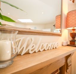 A wooden shelf with a candle in a glass holder a welcome sign and a lamp at West Lodge in Rockbourne