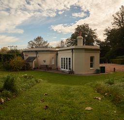 A backyard with a grass lawn and a beige house with white doors and windows at West Lodge in Rockbourne