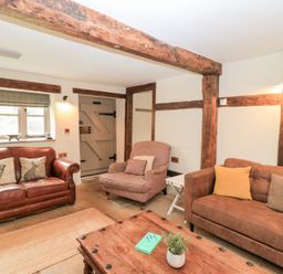 A living room with two sofas an armchair a wooden coffee table and exposed wooden beams at Cosy Cot in Stapleford