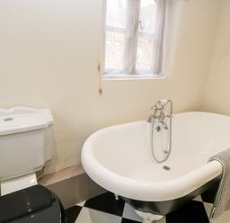 A bathroom with a freestanding clawfoot bathtub a toilet with a black seat and a window at Cosy Cot in Stapleford