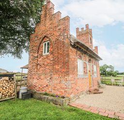 A brick building with a wooden door and stone pathway at The Shooting Folly in Cheswardine