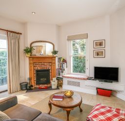 A living room with a fireplace a round wooden coffee table a television and a window seat at East Lodge in Rockbourne